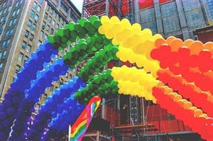 A balloon rainbow with a Pride flag in a city